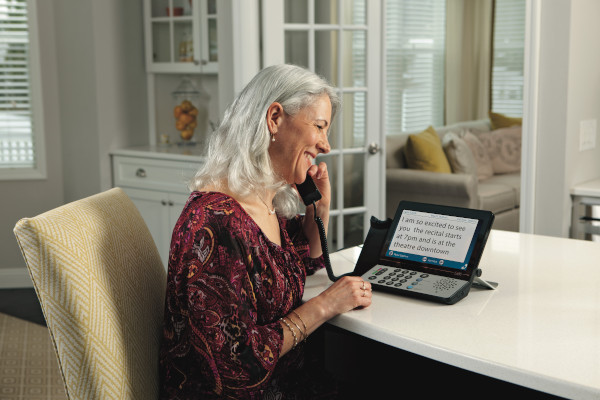 A woman is sitting at her dining room table using a Captel 2400i captioned phone