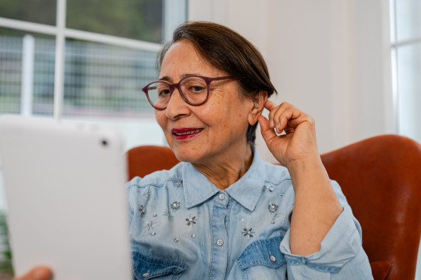 A woman adjusts her hearing aid that is connected to her tablet device