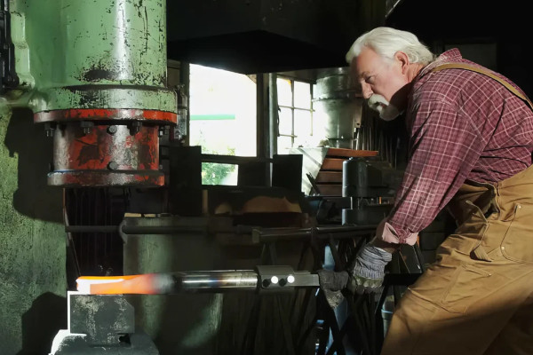 Man shaping heated steel in a hydraulic press